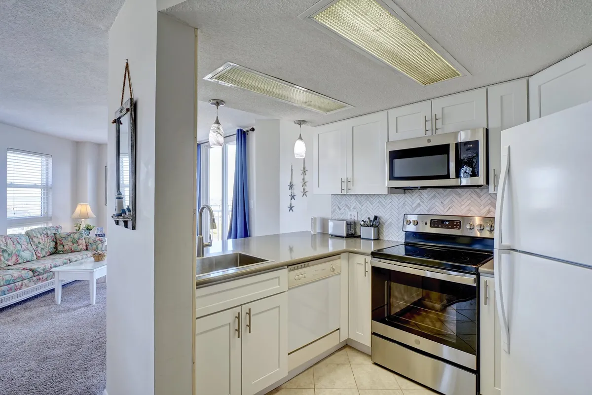 A bright, modern kitchen featuring clean white cabinetry, contemporary light fixtures, ample countertop space, and up-to-date appliances. The space is organized to encourage cooking and gathering, with comfortable sightlines that invite connection and conversation.
