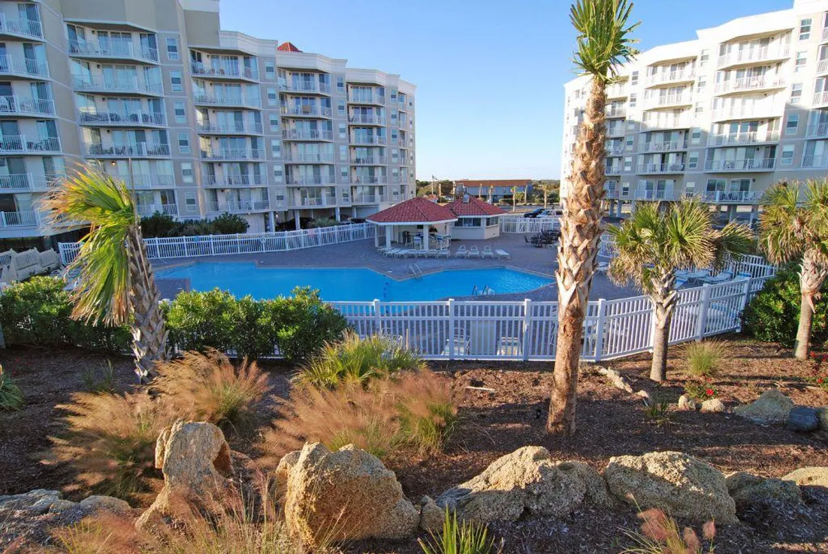 A sparkling swimming pool surrounded by palm trees and resort buildings, with a poolside cabana inviting guests to relax. The setting exudes a sense of leisure, comfort, and vacation ambiance, perfect for both morning swims and evening gatherings.