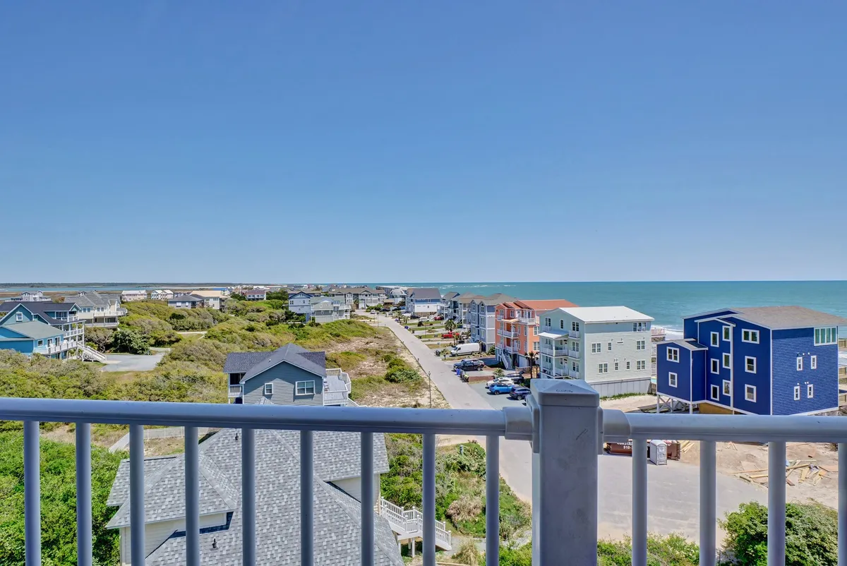 This image showcases a sweeping ocean view framed by colorful coastal homes and lush green vegetation, with a quiet road winding towards the beach. The scene evokes a sense of tranquility and the promise of leisurely beach walks, vibrant sunsets, and relaxation.