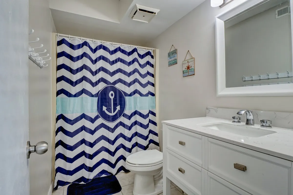 A cheerful bathroom features an anchor-themed shower curtain, white vanity, and decorative wall hangings, radiating a fresh and inviting ambiance.