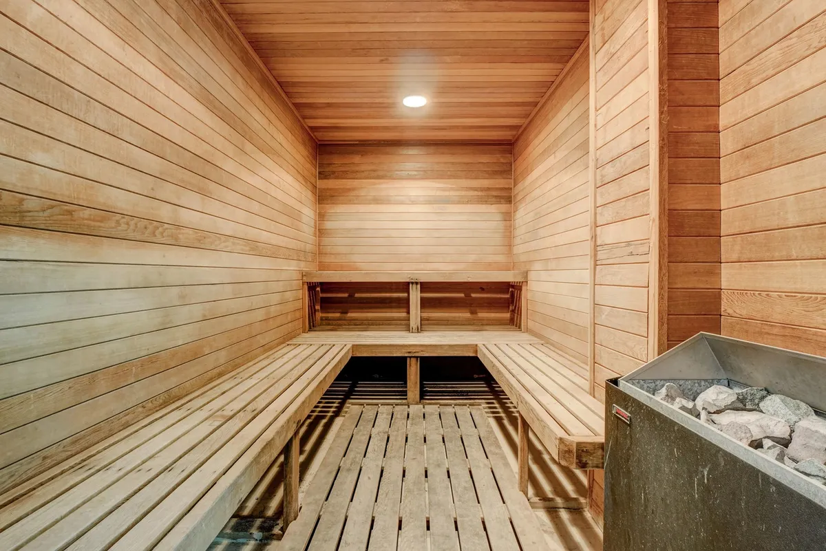 A serene sauna room featuring wooden benches, a stone heater, and warm wooden paneling. The tranquil ambiance invites relaxation and self-care—a peaceful retreat within the resort complex.