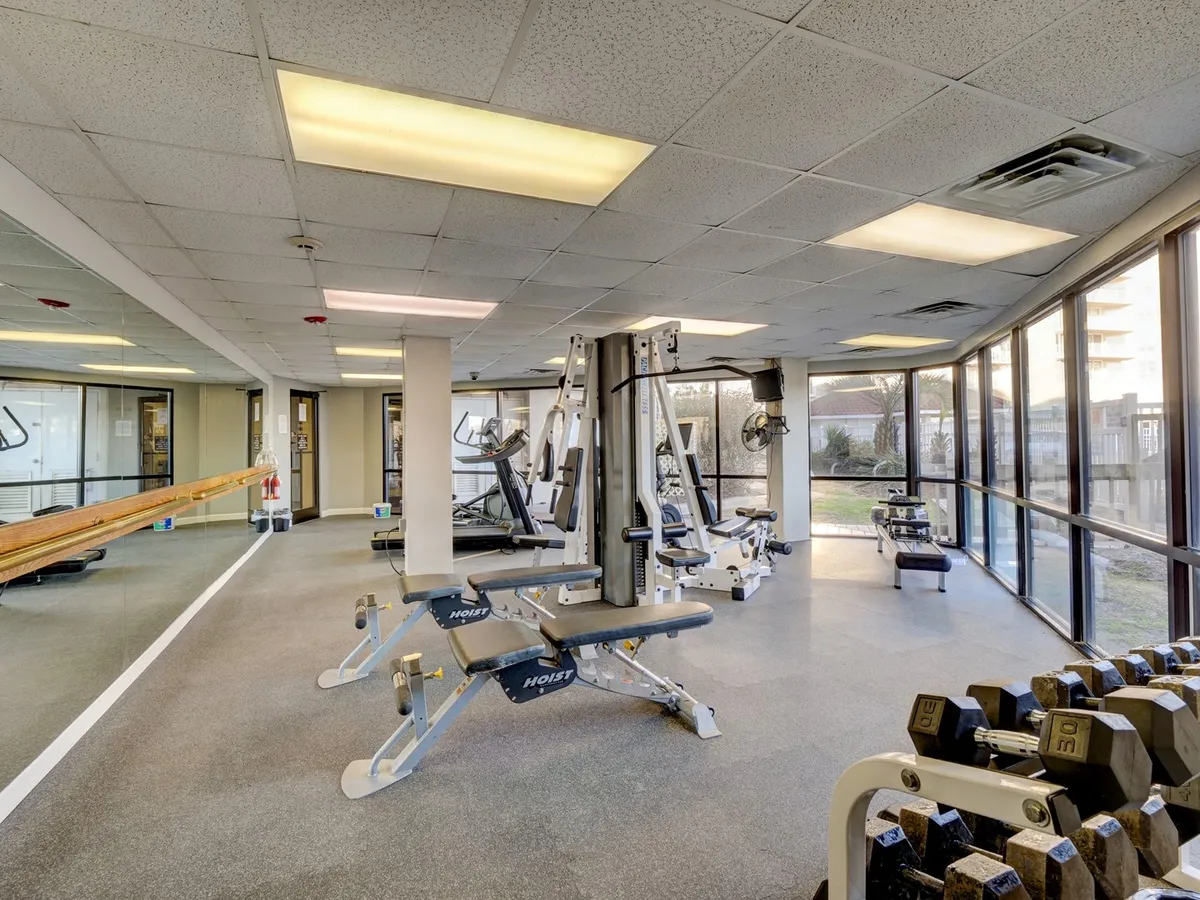 A bright, motivational fitness center featuring a variety of weight machines, dumbbells, large windows letting in natural light, and exercise mats. The space is modern, well-equipped, and inviting for both cardio and strength training.