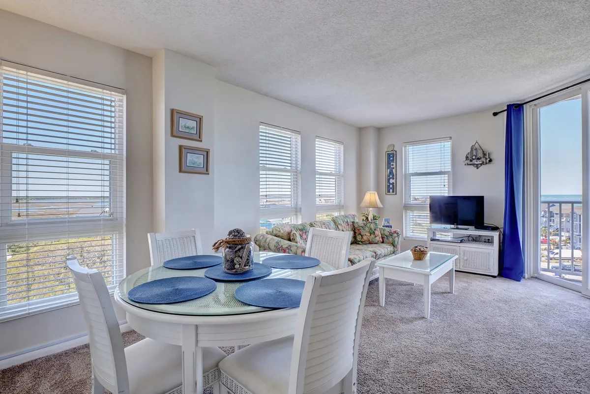 A cozy dining area featuring a dining table set near windows that offer views of the outdoors, adjacent to a comfortable sofa and television. Natural light streams in, creating a warm ambiance perfect for family meals and relaxed evenings.